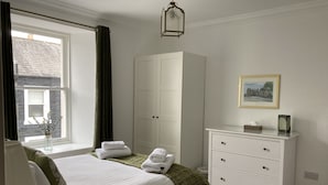Ein Schlafzimmer mit Bett, Kleiderschrank, Kommode, einem Fenster mit Vorhängen und einer Pendelleuchte.