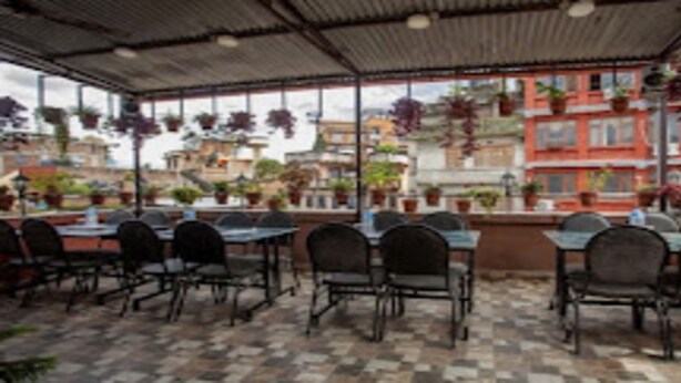 An outdoor patio with tables and chairs, surrounded by buildings with balconies and hanging plants. - MeroStay 127 Divine Guest House (Kathmandu)