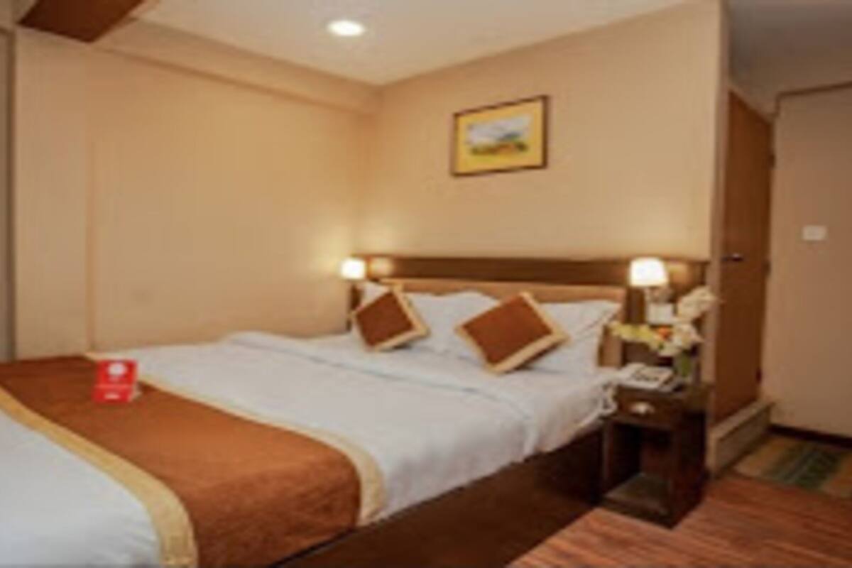 Ein Hotelzimmer mit Bett, Nachttisch, Lampe und einem Gemälde an der Wand.