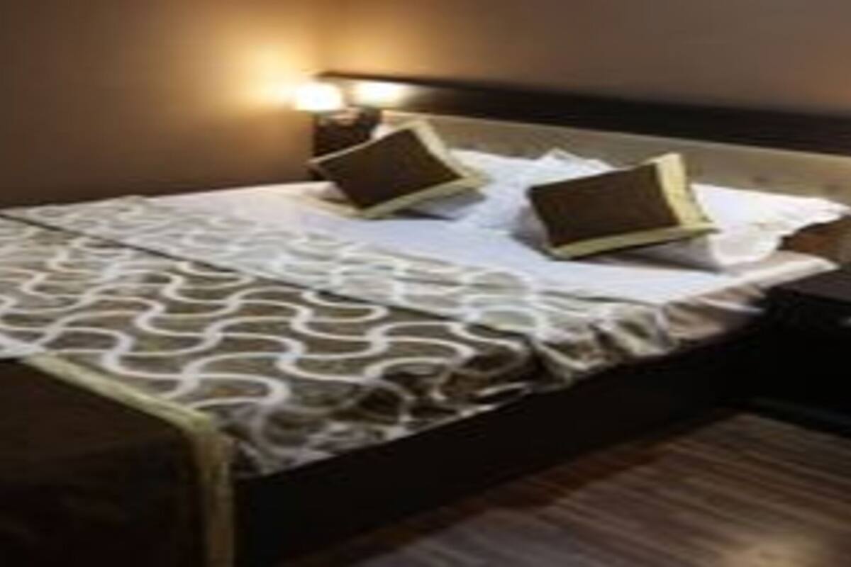 Ein ordentlich bezogenes Bett mit einem gemusterten Überwurf, zwei Kissen und einem Nachttisch mit einer Lampe.