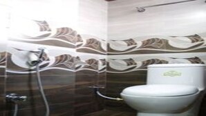 A bathroom with a toilet, a shower, and a wall with a leaf pattern. - MeroStay 127 Divine Guest House (Kathmandu)
