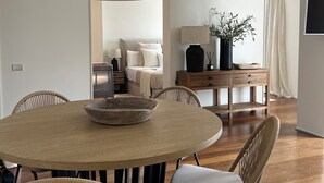 Uma área de jantar com uma mesa redonda de madeira, cadeiras de vime, um lustre grande e um aparador de madeira com uma planta.
