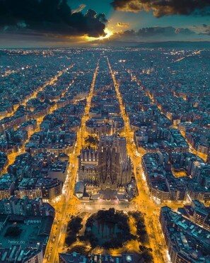 An aerial view of a cityscape with a prominent cathedral at the center, surrounded by dense urban development and illuminated streets. - Best Location Apartment, in the Most Luxurious Street in Barcelona (Barcelona)