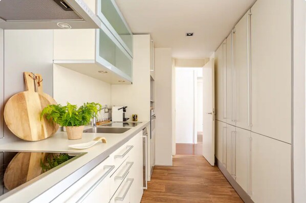 A modern kitchen with white cabinetry, a wooden cutting board, and a potted plant. - Best Location Apartment, in the Most Luxurious Street in Barcelona (Barcelona)