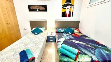 Una habitación pequeña y bien iluminada con dos camas, un armario, un equipo de aire acondicionado y obras de arte en las paredes.