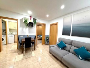 Un espace de vie compact comprenant un coin repas, une kitchenette et un canapé agrémenté de coussins turquoise.
