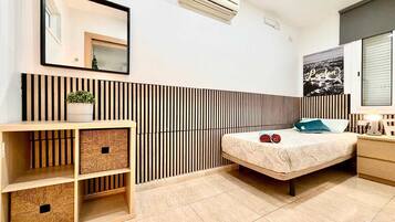 Un dormitorio moderno con cama, mesita de noche, lámpara, equipo de aire acondicionado, espejo y una pared con listones verticales.