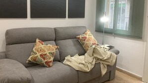 A grey sofa with patterned cushions and a blanket, a floor lamp, and a window with blinds. - Near to Beach and 15 min to Barcelona by Train (Sant Adrià de Besòs)