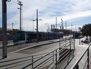 A tram station with a modern design, featuring a covered waiting area and metal safety barriers.