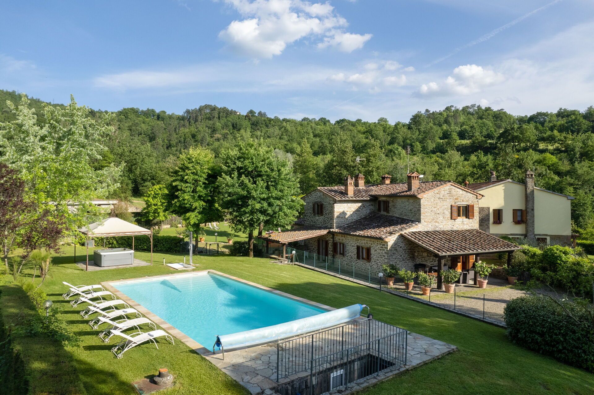 Eine Villa mit Swimmingpool, umgeben von üppiger Vegetation und Hügeln.
