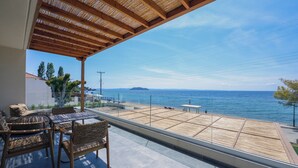 A balcony with wicker furniture, a view of the sea, and a distant island. - Amyntas Seafront Hotel - Adults Only (Sithonia)