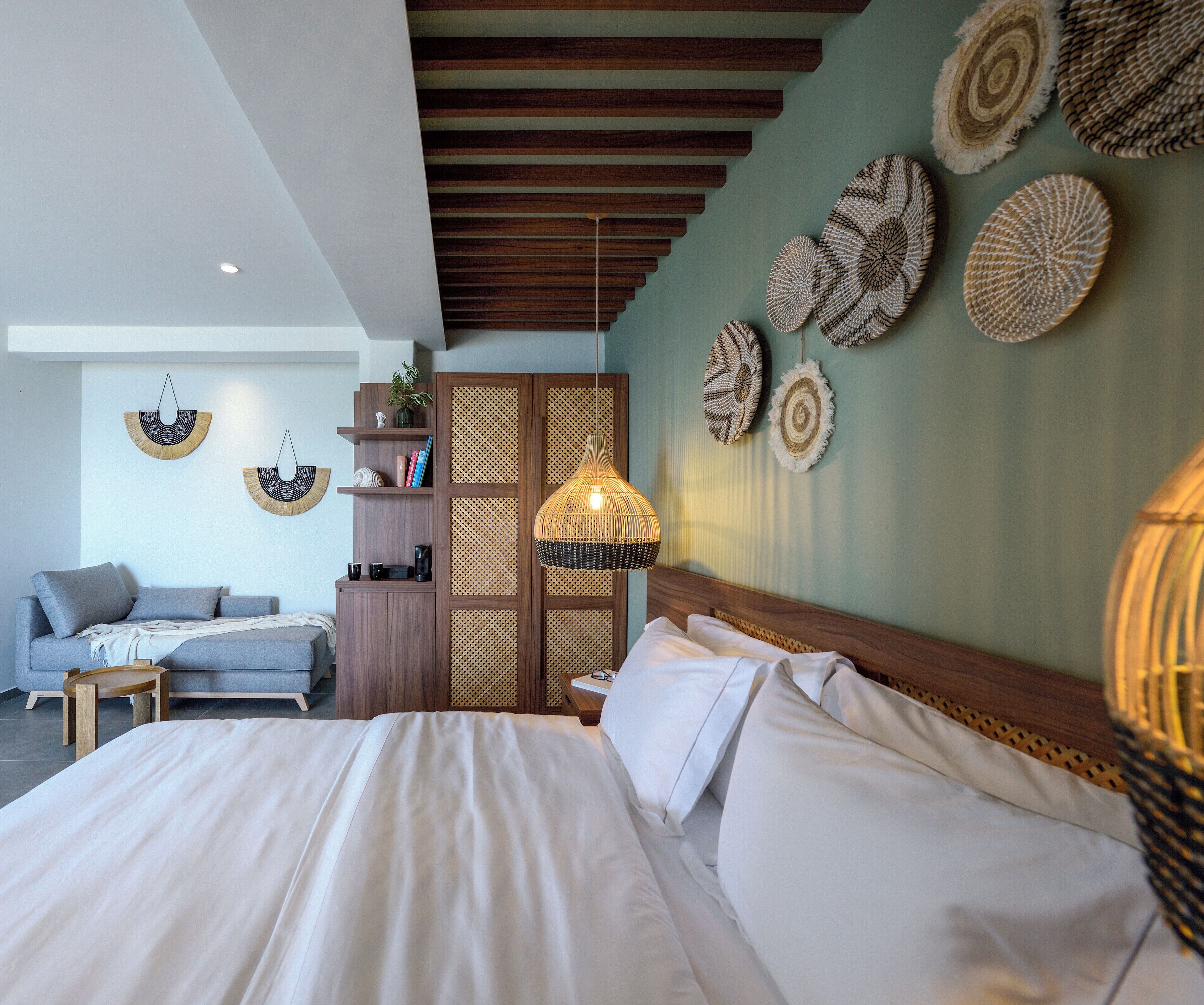 A modern bedroom with a large bed, a wooden headboard, a hanging light fixture, and decorative wall hangings.