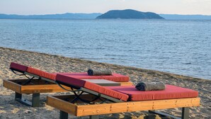 Two wooden sun loungers with red cushions on a sandy beach, overlooking calm water and distant mountains. - Amyntas Seafront Hotel - Adults Only (Sithonia)