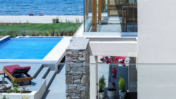 A modern outdoor pool area with a view of the sea, a covered seating area, and a stone wall. - Amyntas Seafront Hotel - Adults Only (Sithonia)