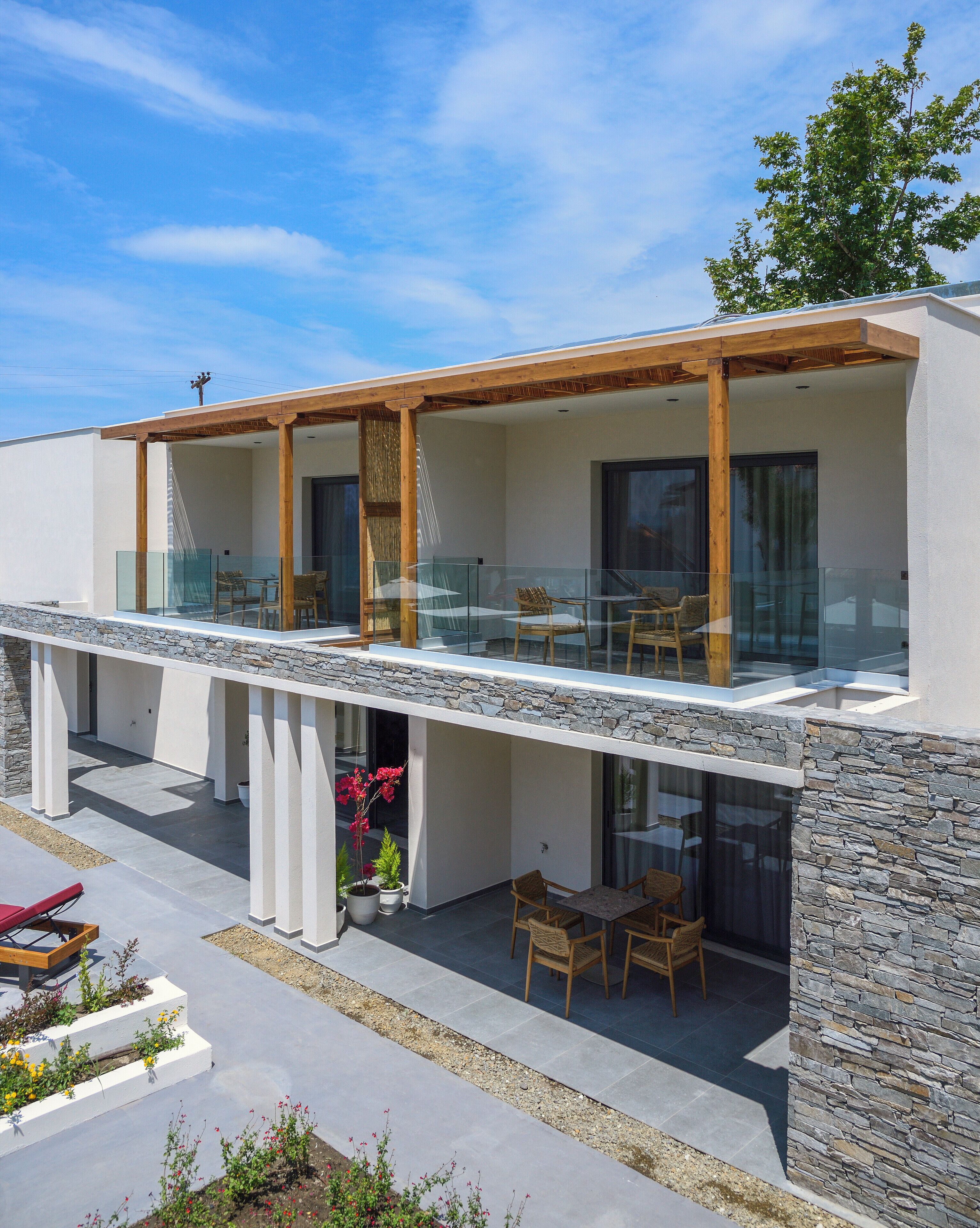 A modern house with a stone facade, a wooden deck, and a glass balustrade.