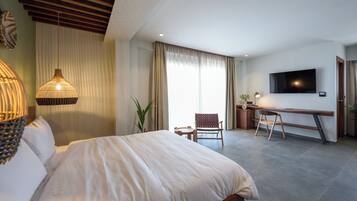 Habitación de hotel con una cama grande, un escritorio con silla, televisor y una planta.