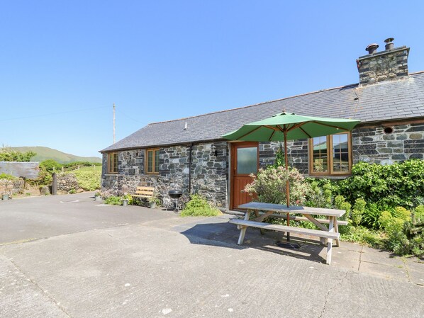 A stone building with a wooden door, a green umbrella, and a picnic table. - Swn y Nant (Tywyn)