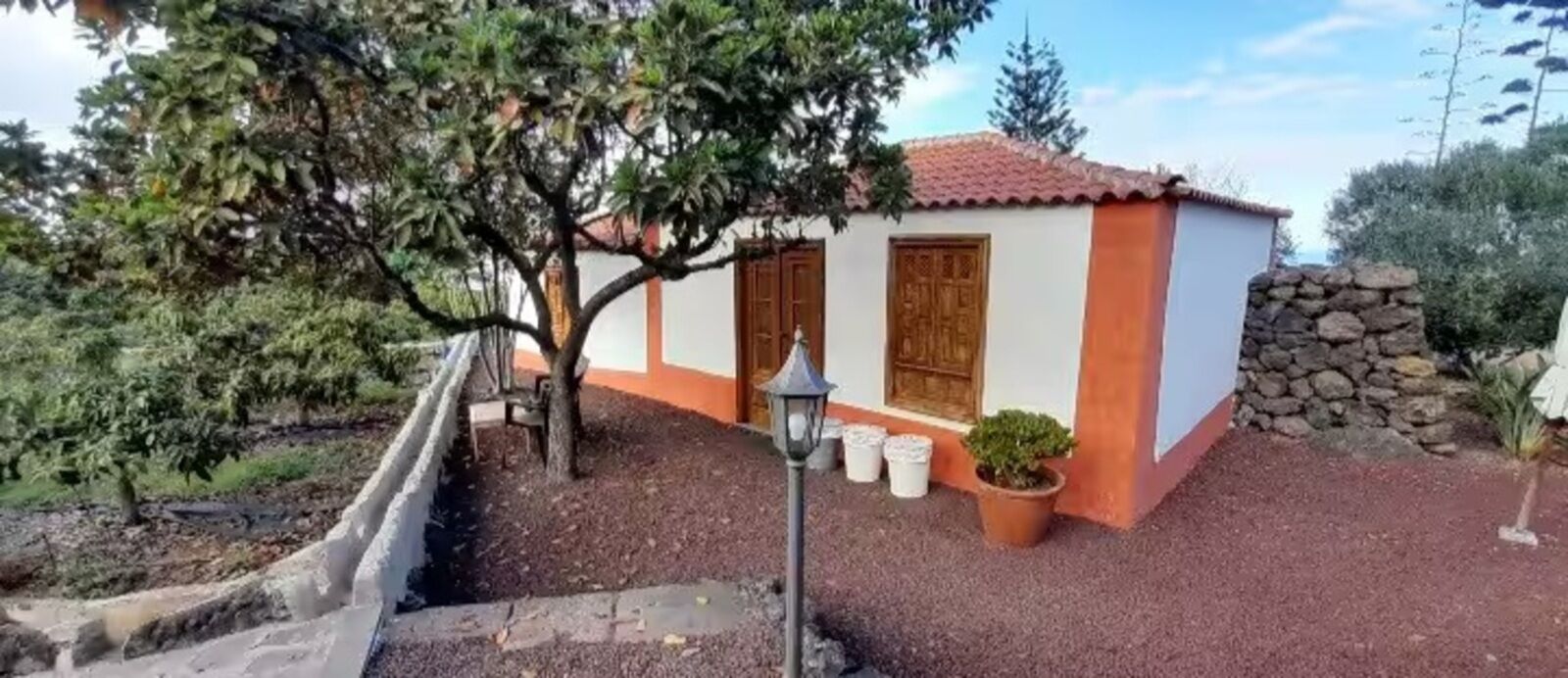 A small building with a tiled roof, a stone wall, and a tree in front.
