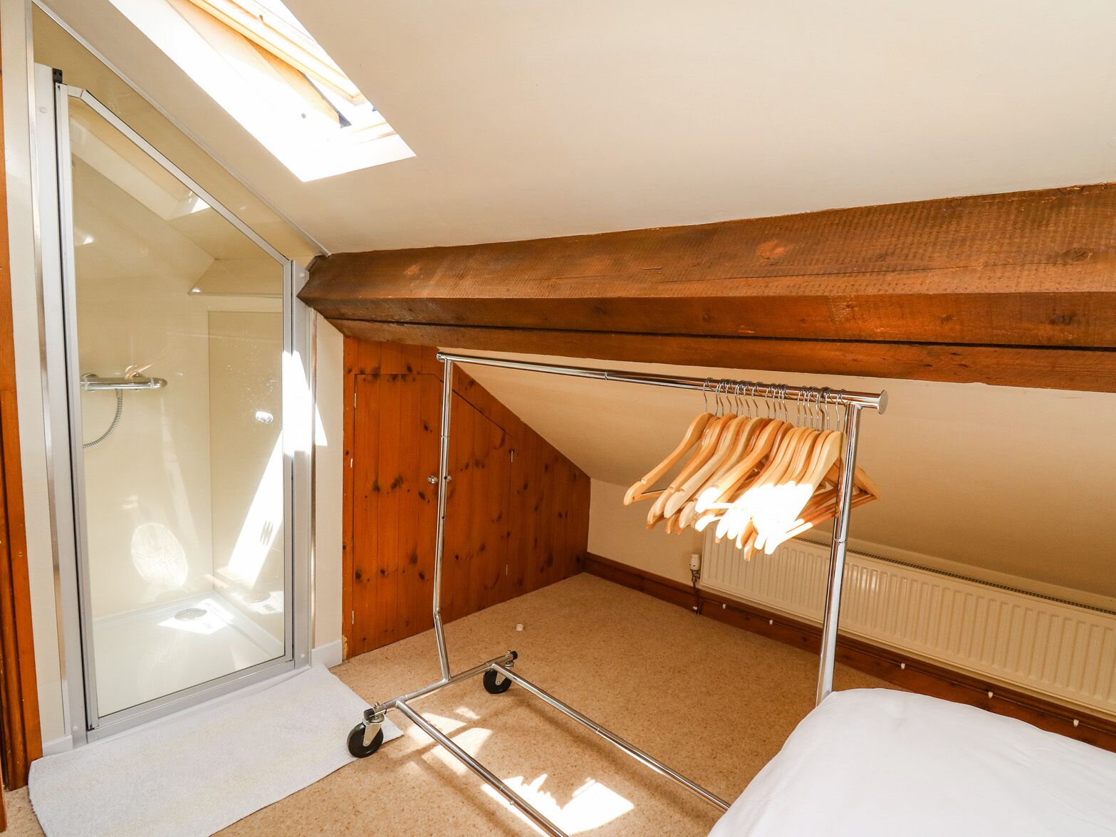 A bedroom with a skylight, a shower, wooden walls, a bed, and a clothes rack.