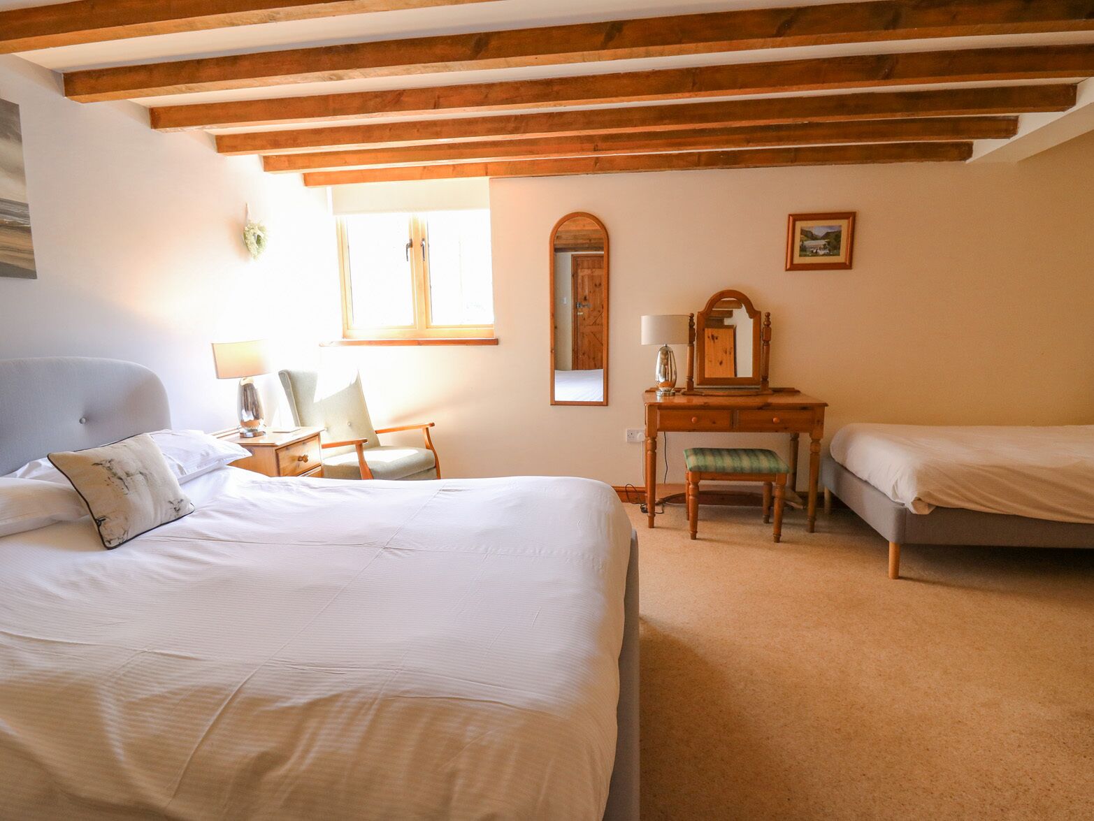 A bedroom with a large bed, a chair, a desk with a mirror, and a window.