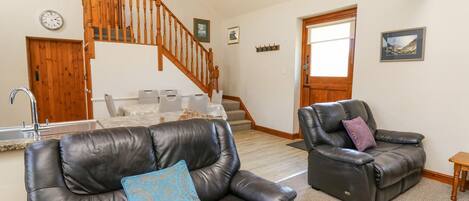 A spacious living area with a staircase, leather sofas, and a kitchen area.