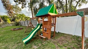 Una estructura de juego de madera con un tobogán verde y un techo pequeño.