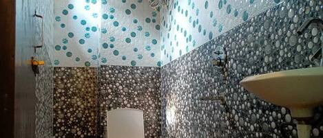 A bathroom with a toilet, sink, and red bucket. The walls are decorated with patterned tiles.