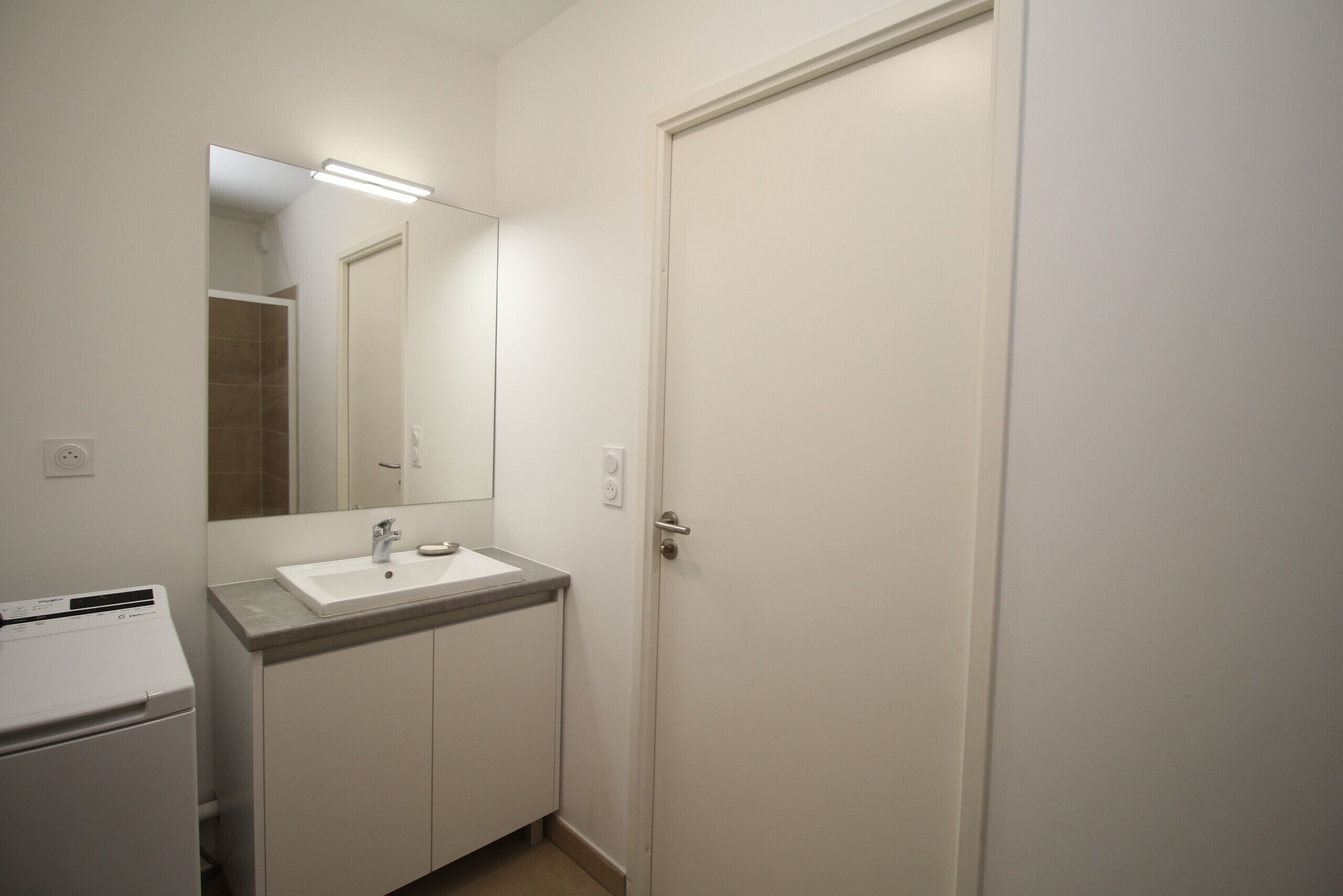 A small, clean bathroom with a white sink, mirror, and a closed door.