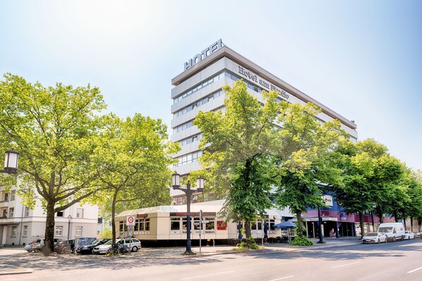 Un hotel a più piani con un evidente cartello con la scritta 'HOTEL', immerso nel verde e circondato da auto parcheggiate.