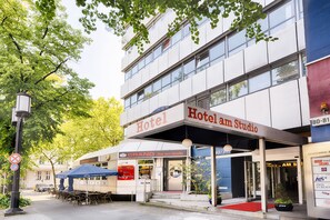 Un hotel con facciata moderna, area salotto esterna e ingresso con tappeto rosso.