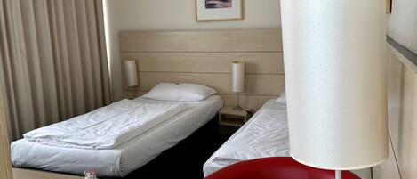 Habitación de hotel con dos camas, un escritorio con lámpara, una silla roja y un cuadro en la pared.