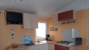 A compact kitchen with a gas stove, a sink, and a microwave. There is a small dining table and a window providing natural light.