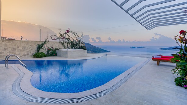 A swimming pool with a clear view of the sea and distant mountains, surrounded by a modern architectural structure.