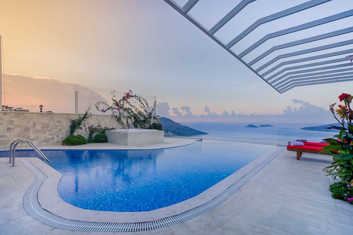 A swimming pool with a clear view of the sea and distant mountains, surrounded by a modern architectural structure.