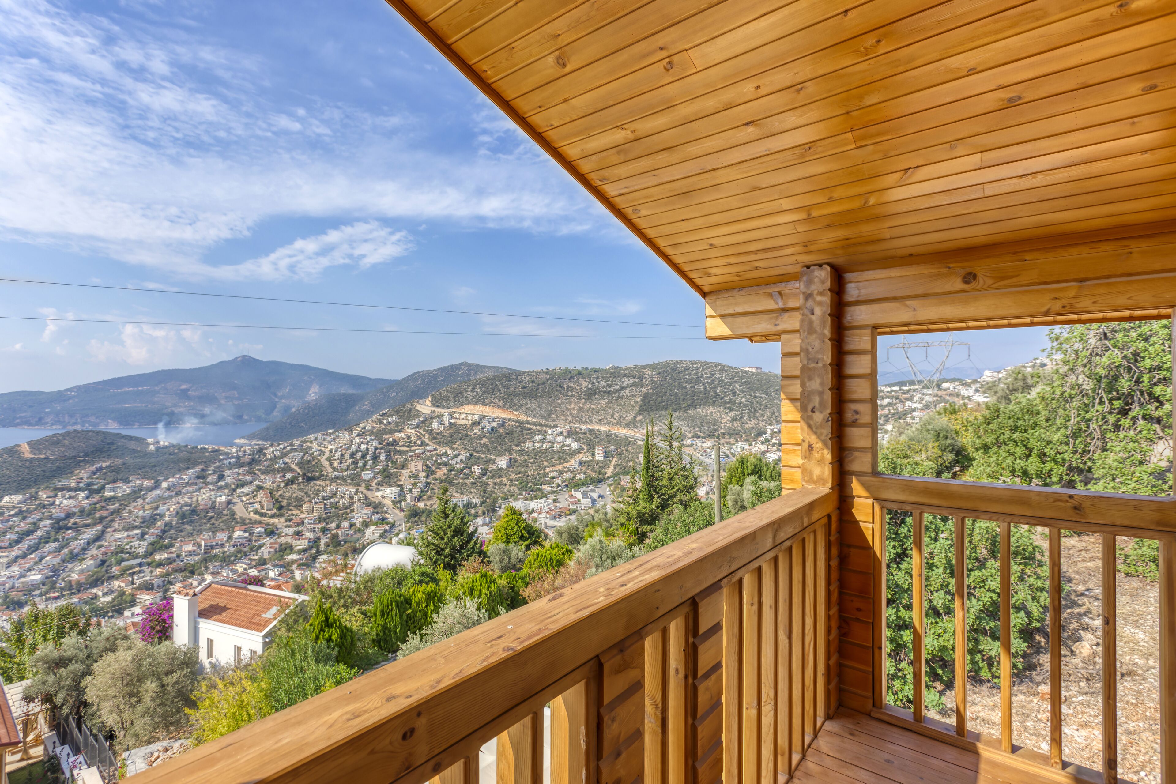 A wooden balcony with a view of a coastal town and mountains.