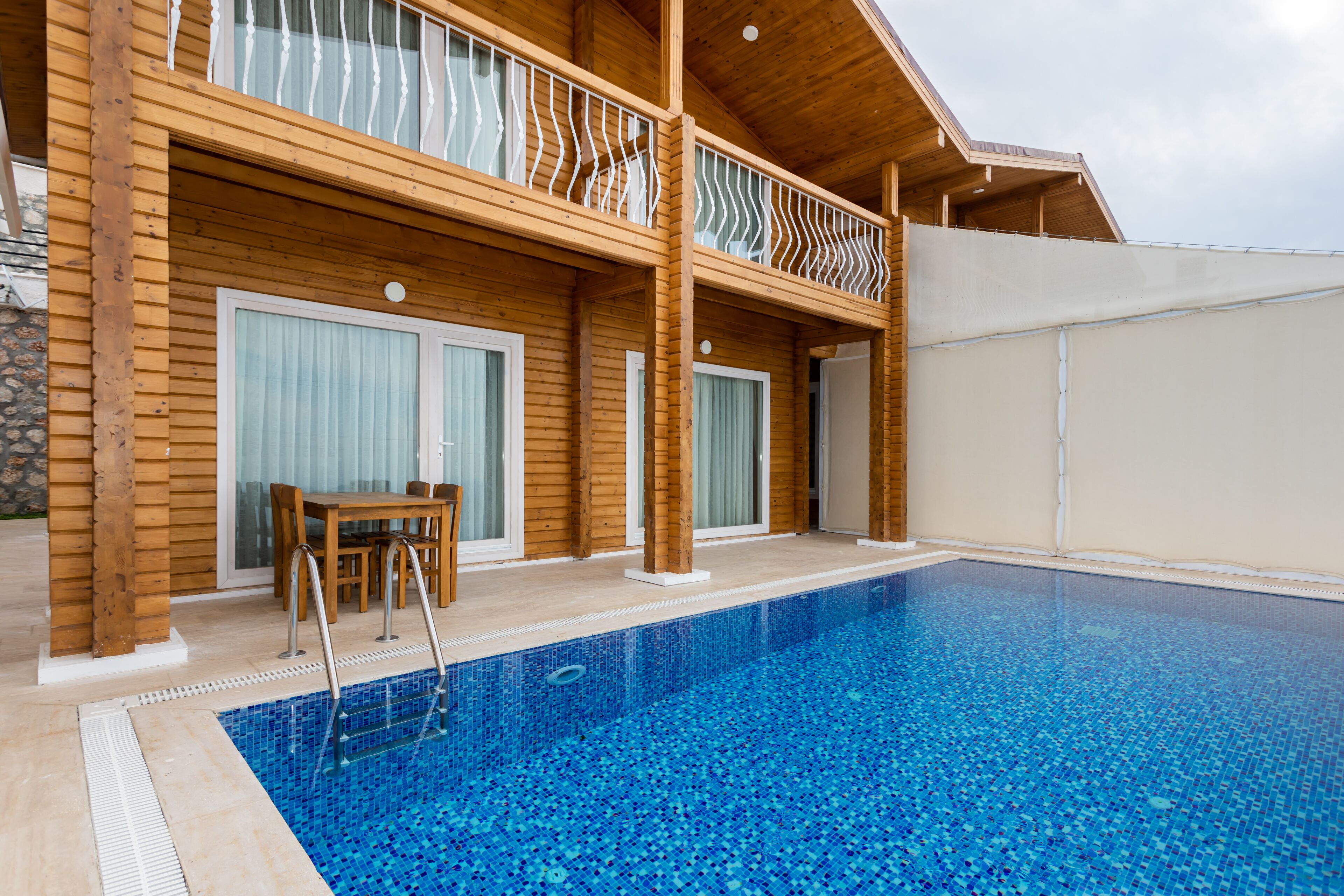 Ein Holzhaus mit Swimmingpool, Balkon und Essbereich.