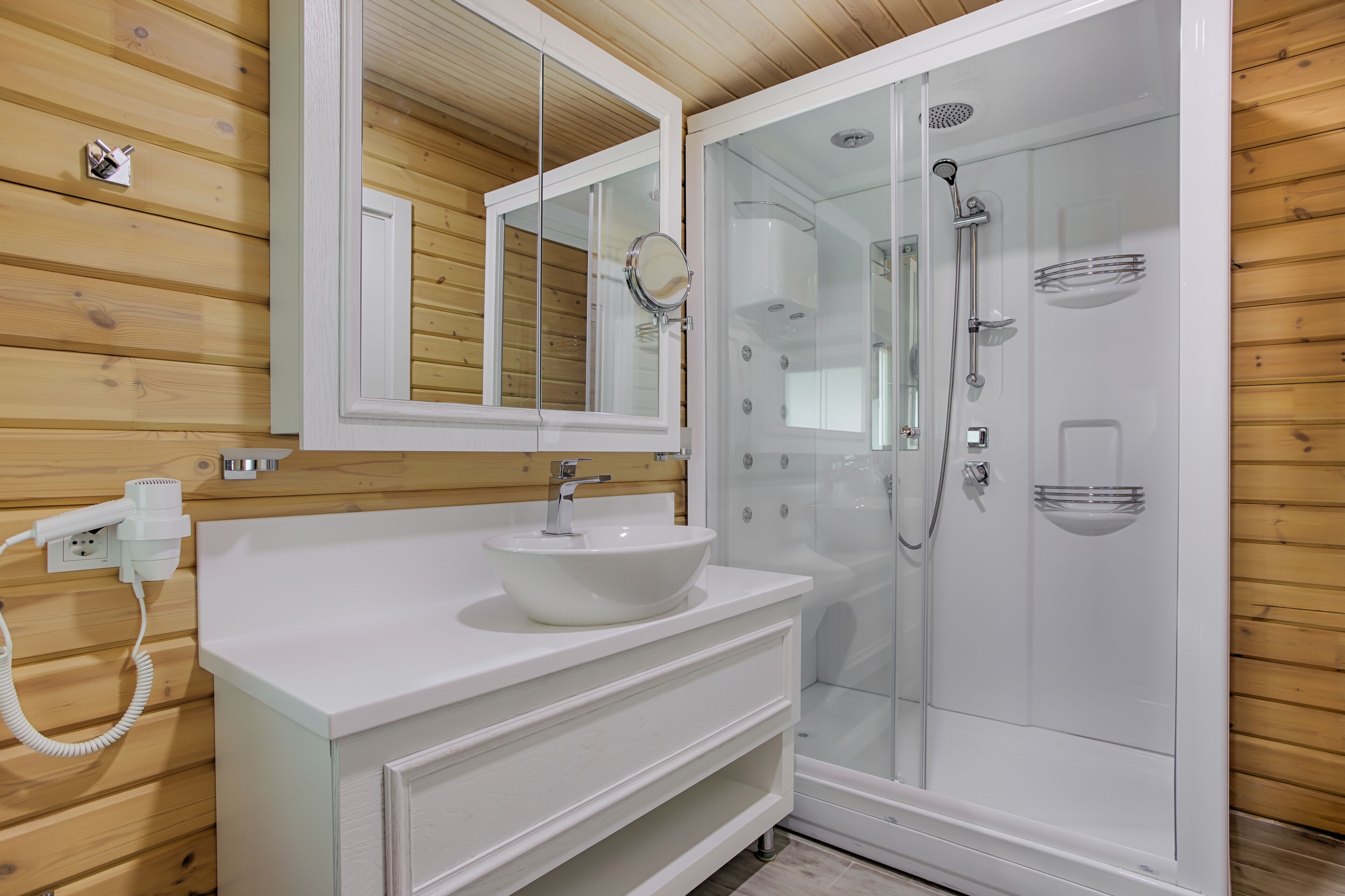 A modern bathroom with a white sink, mirror, and glass-enclosed shower.
