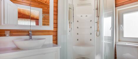 Un baño moderno con ducha de vidrio, lavamanos blanco y techo de madera.