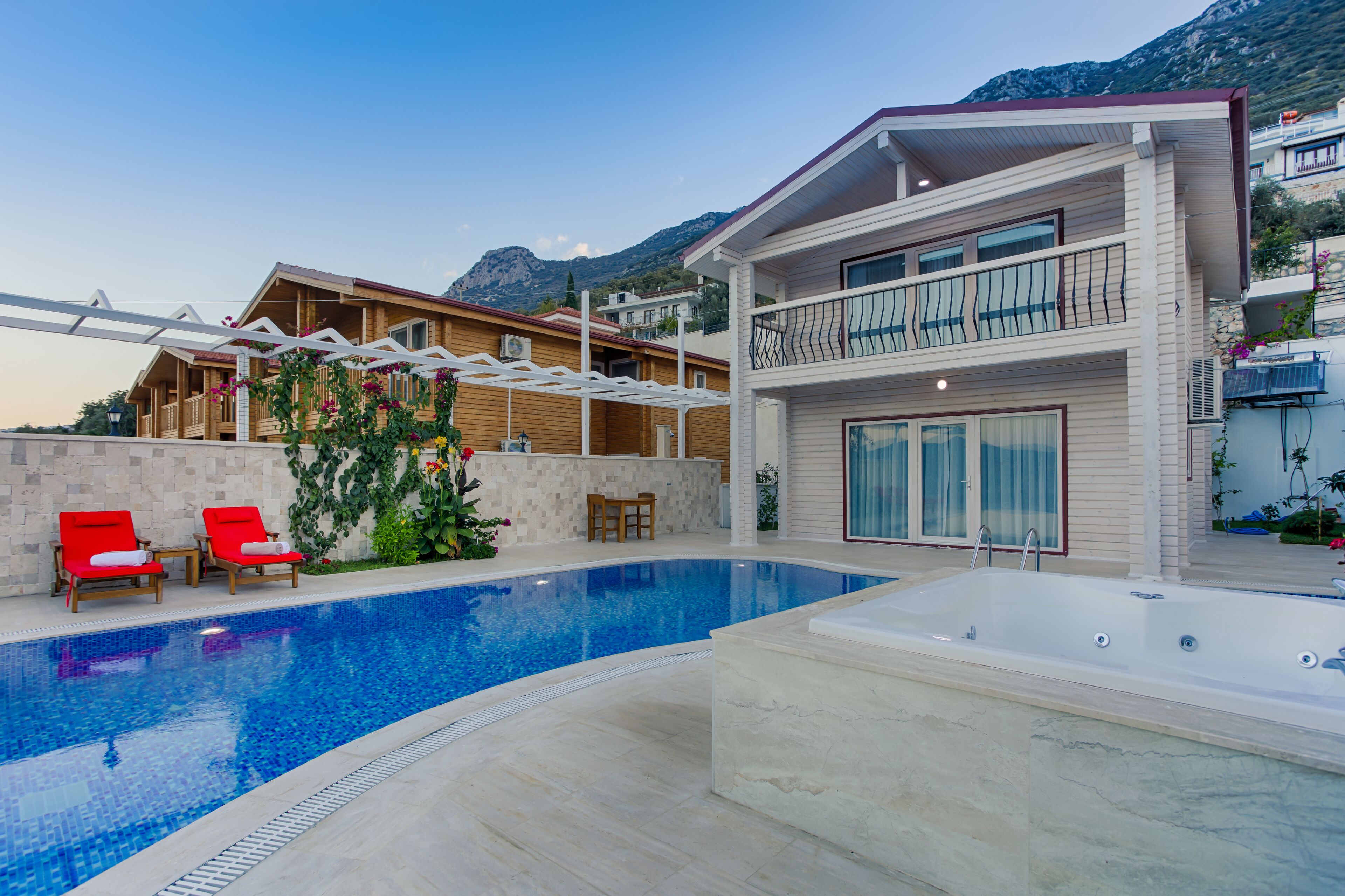 A modern two-story house with a swimming pool, red lounge chairs, and a balcony.