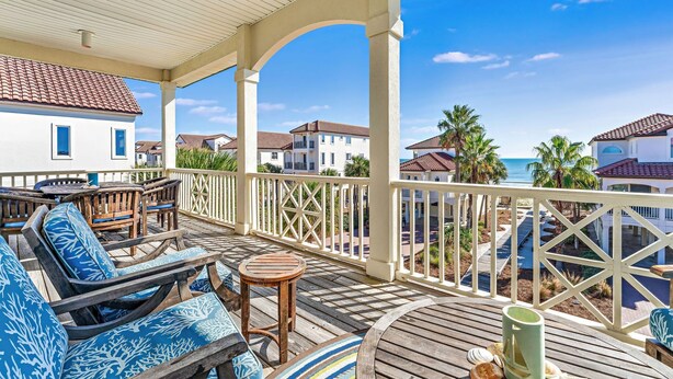 A covered outdoor area with wooden furniture, a view of the ocean, and a white building in the background. - Southern Star - Across Street From Beach, Bay Views. Community Pool! (St George Island)