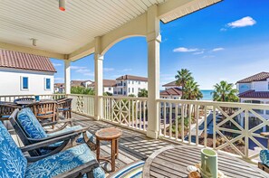 A covered outdoor area with wooden furniture, a view of the ocean, and a white building in the background. - Southern Star - Across Street From Beach, Bay Views. Community Pool! (St George Island)