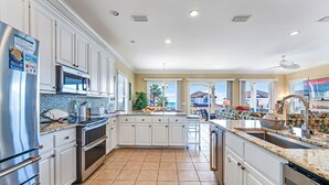 A spacious kitchen with white cabinets, stainless steel appliances, and a large island with a sink. - Southern Star - Across Street From Beach, Bay Views. Community Pool! (St George Island)