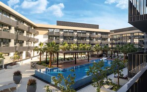 A rooftop pool area with a modern pool, lounge chairs, and palm trees. - Opulent 1BR at Belgravia Tower JVC by Deluxe Holiday Homes (Dubai)