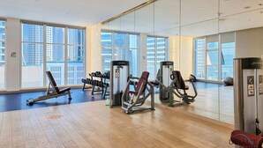 A spacious gym with various exercise equipment, large windows, and a wooden floor. - Elegant Studio at DAMAC Privé Business Bay by Deluxe Holiday Homes (Dubai)