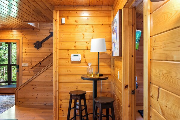 A wooden cabin interior with a staircase, a table with a lamp, and a window.