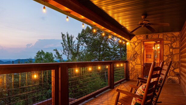A wooden deck with a stone wall and a view of trees. There are string lights and a ceiling fan. - Mountain View! Cabin, 6BR, Yard, Firepit, GameRoom (Sevierville)