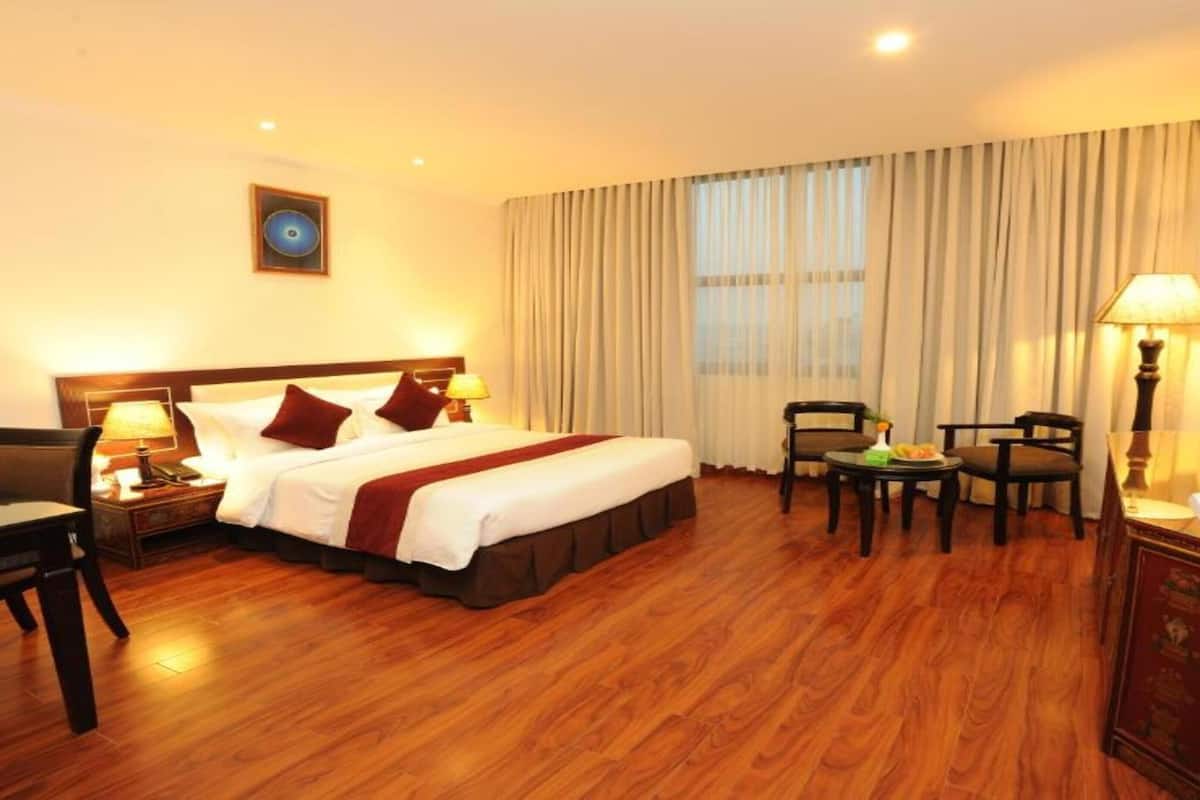A hotel room with a bed, a desk, a chair, a small table, and a TV.