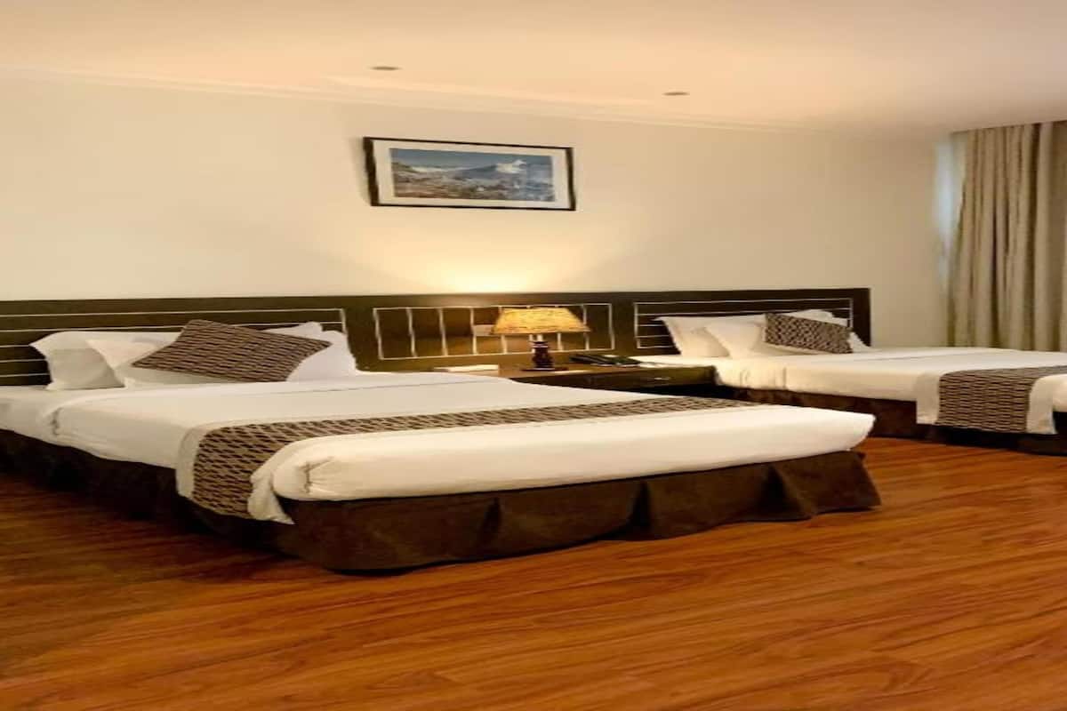 A hotel room with two beds, a nightstand, a lamp, and a window with curtains.
