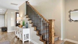 A staircase with wooden steps and black balusters, a white console table with decorative items, and a light-colored wall with a decorative mirror.