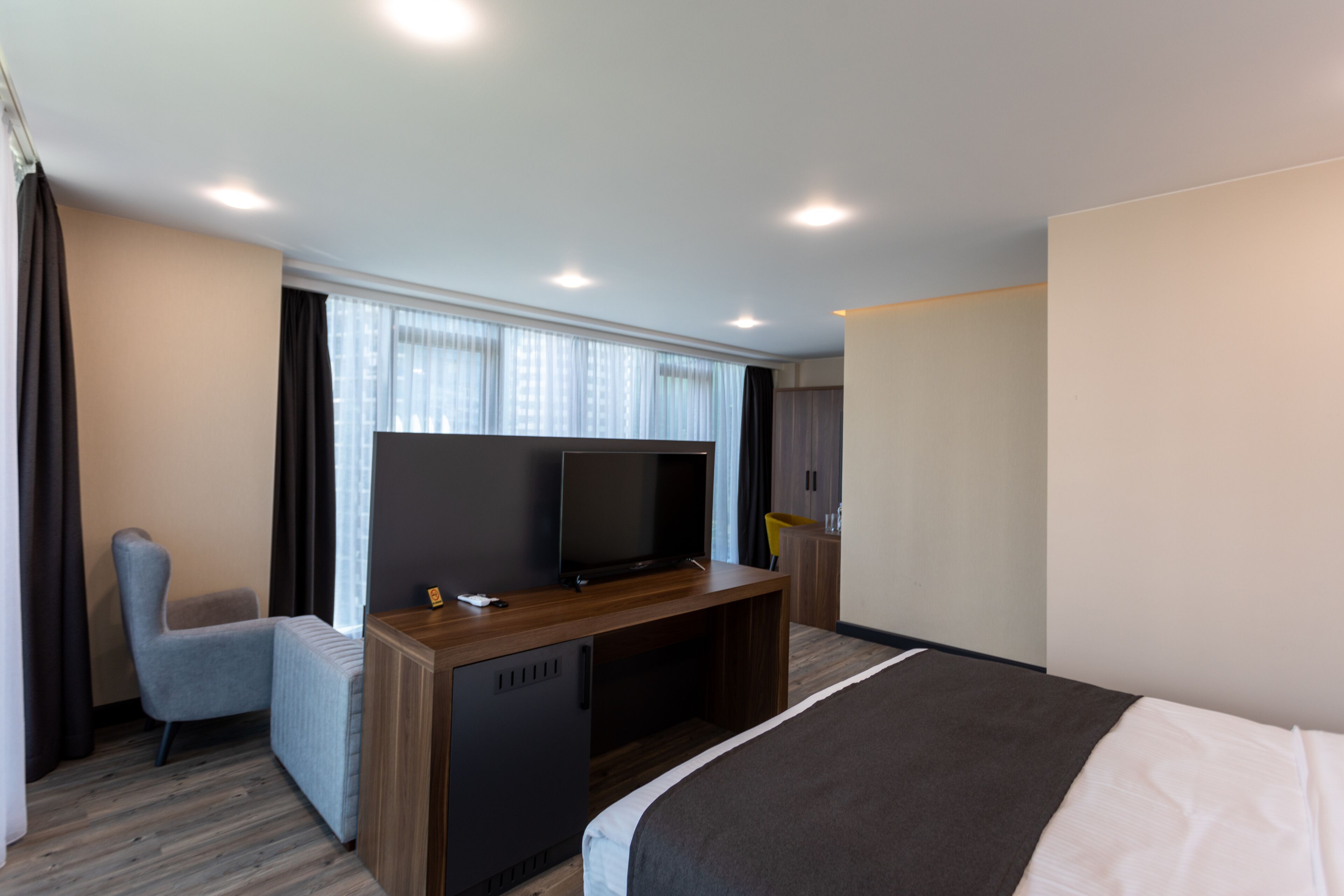 A hotel room with a bed, a TV on a wooden stand, a chair, and a desk.